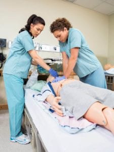 Nurses performing CPR on dummy patient in hospital room